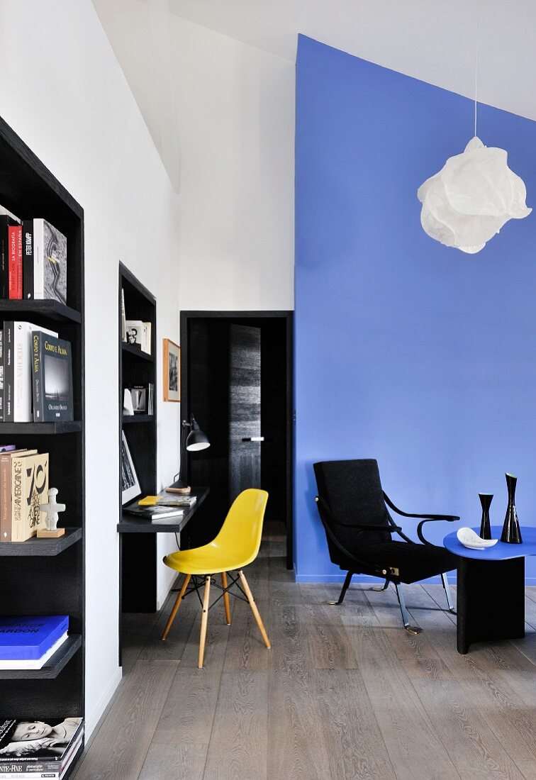 Schwarze Einbauregale, Konsolentisch mit gelbem Stuhlklassiker und blauer Raumteiler im Wohnbereich