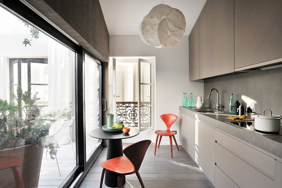 Küchenzeile und kleiner, runder Tisch mit Designerstühlen vor Glasschiebetür