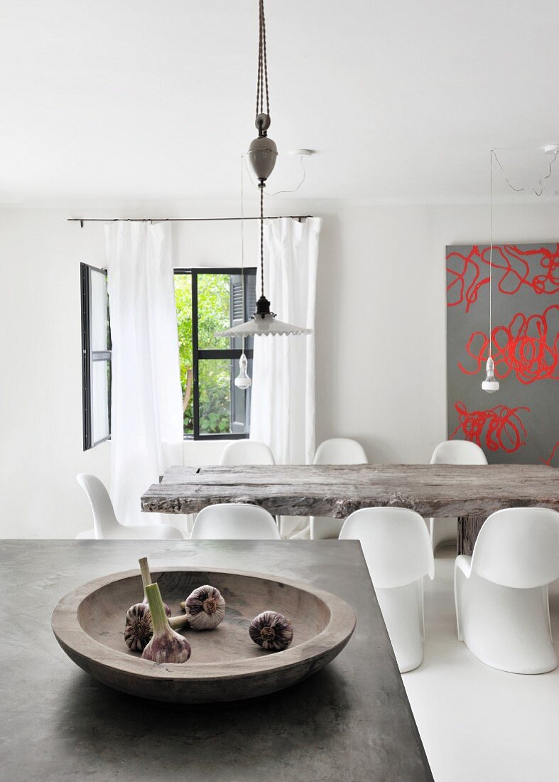 Holzschale mit Knoblauchknollen auf Betonküchentheke vor rustikalem Esstisch mit weißen Stuhlklassikern