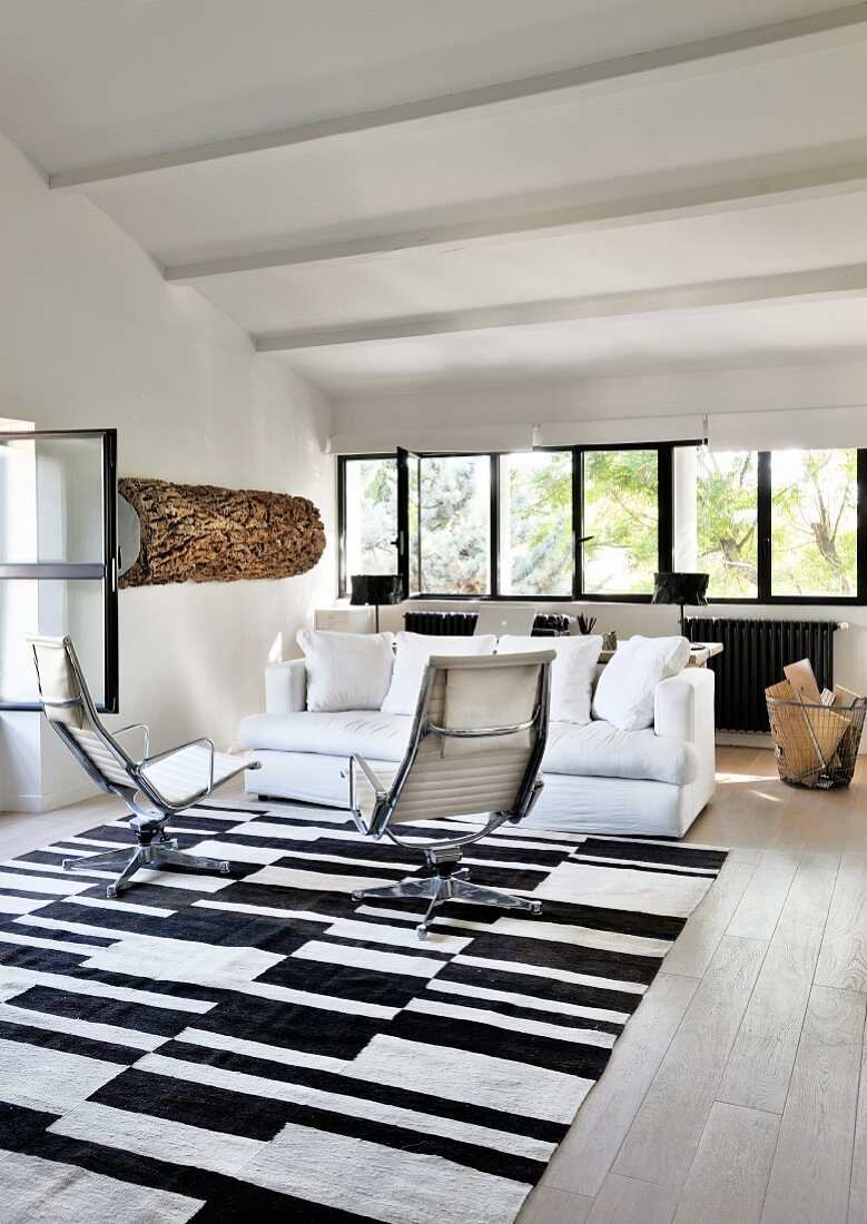 Loungebereich mit weißer Polstercouch und Armlehnsesseln auf schwarz-weißem Teppich