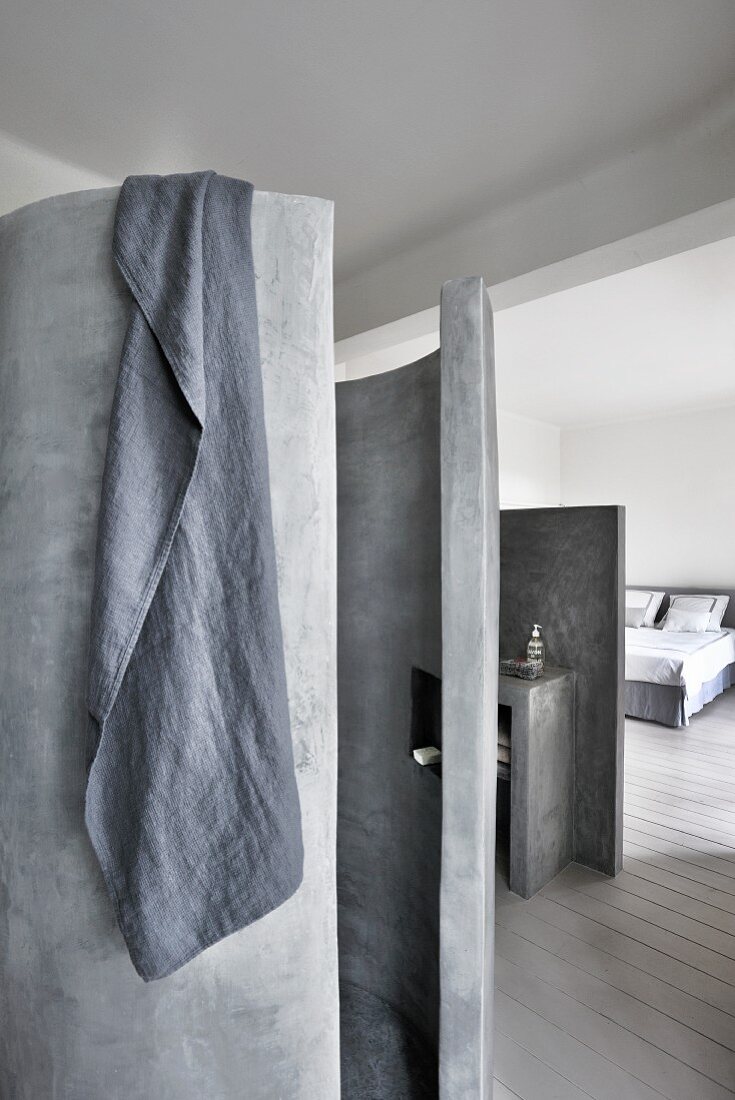 Grey towel hung over concrete cylindrical shower and view into bedroom
