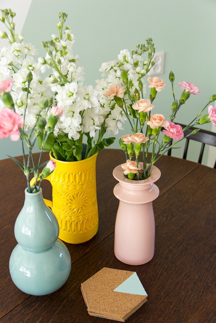 Verschiedenfarbige Vasen mit Blumen und Korkuntersetzer
