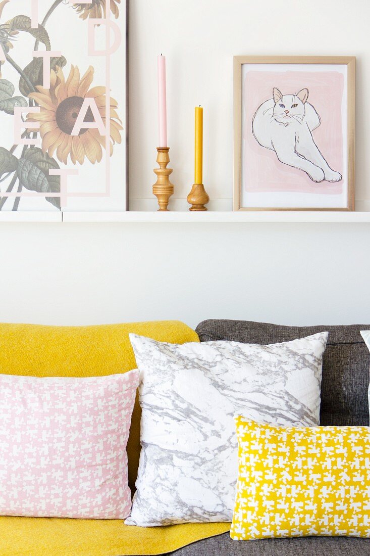 Musterkissen in Rosa und Gelb auf dem Sofa unter einer Bilderleiste