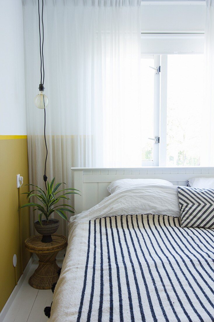 Schwarz-weiß gestreifte Decke auf dem Bett vor dem Fenster