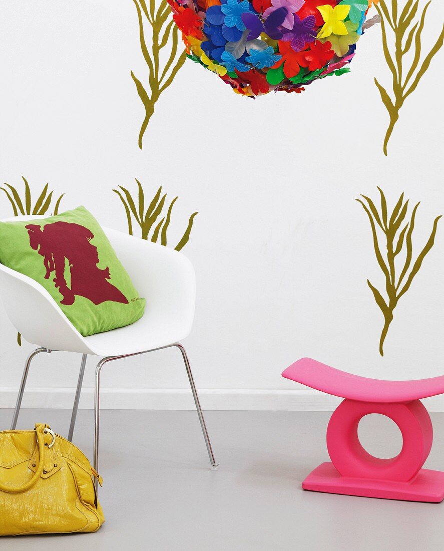 DIY-Wandgestaltung mit grünem Schablonenmuster, davor weißer Armlehnstuhl mit Kissen, gelber Ledertasche und rosa Schemel