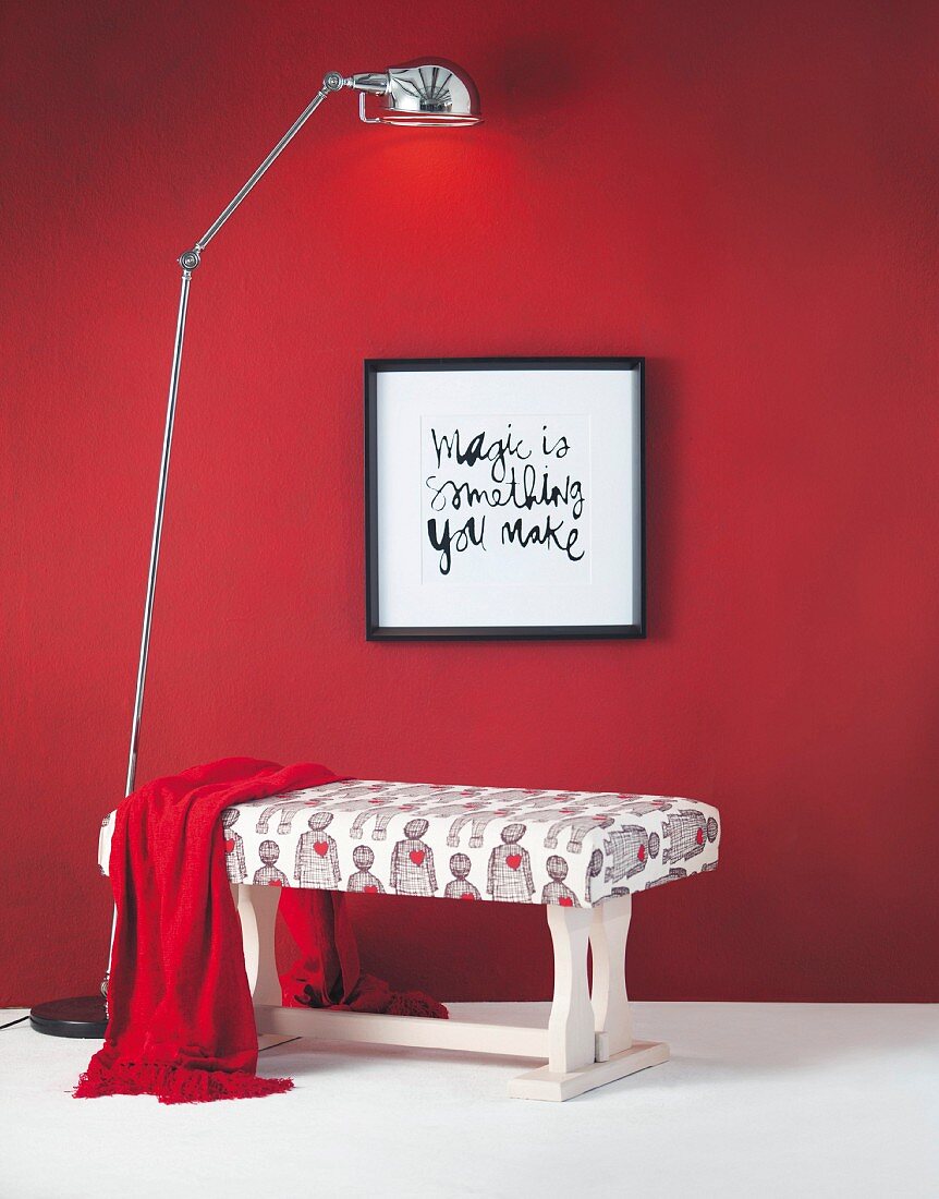 DIY-Sitzbank aus früherem Holzcouchtisch vor roter Wand mit Sinnspruch und Stehleuchte arrangiert