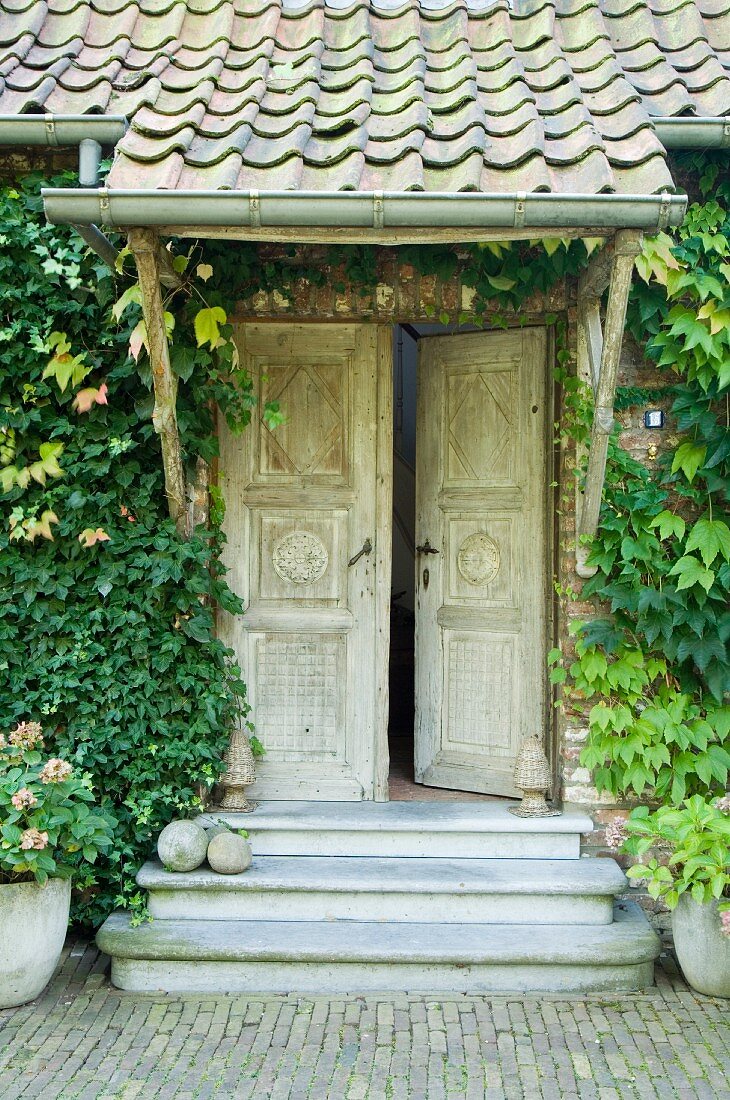 Vintage Eingang mit traditionellen geschnitzten Holztüren, Vordach und begrünter Fassade