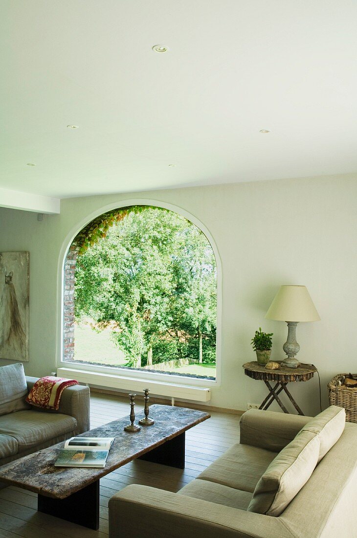 Gemütliche Lounge mit rustikalem Couchtisch und sommerlichem Gartenblick durch Rundbogenfenster