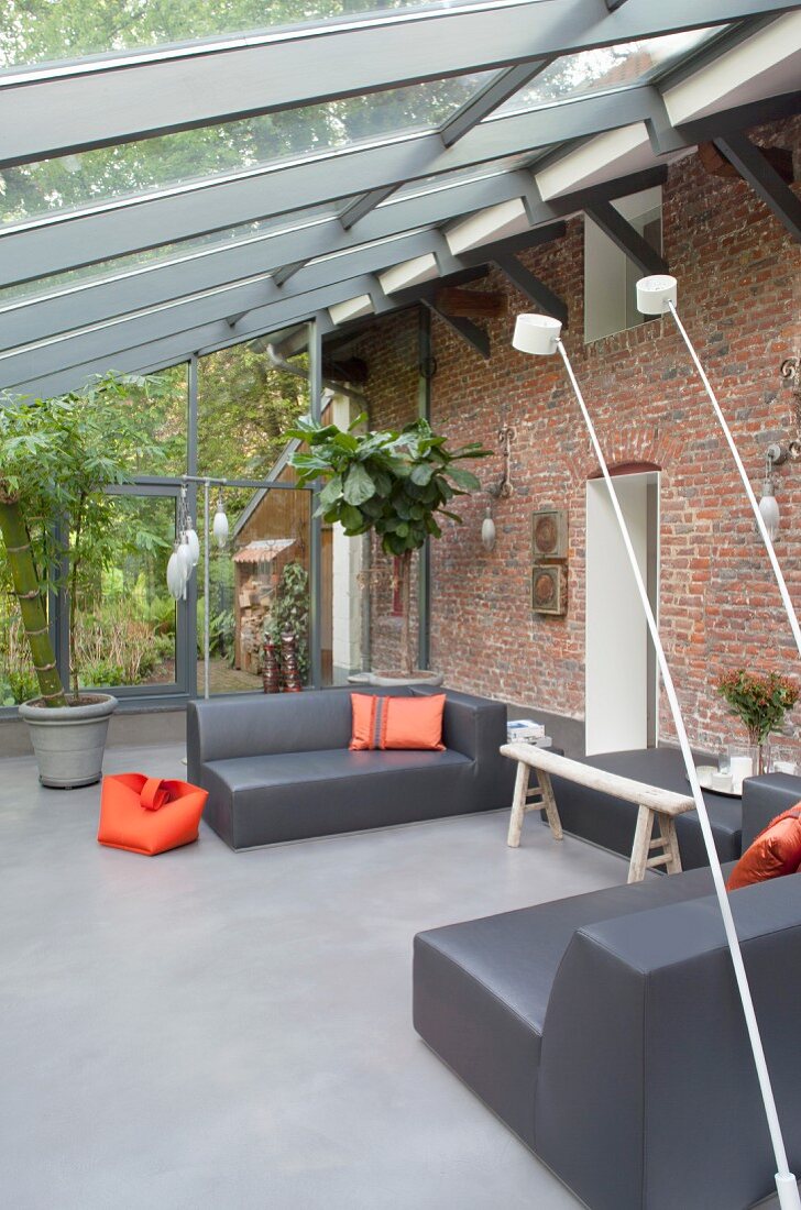 Grey designer lounge furniture and orange accents in conservatory extension on rustic brick façade