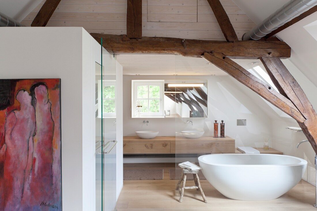 Bathroom behind glass wall in converted attic with rustic roof beams