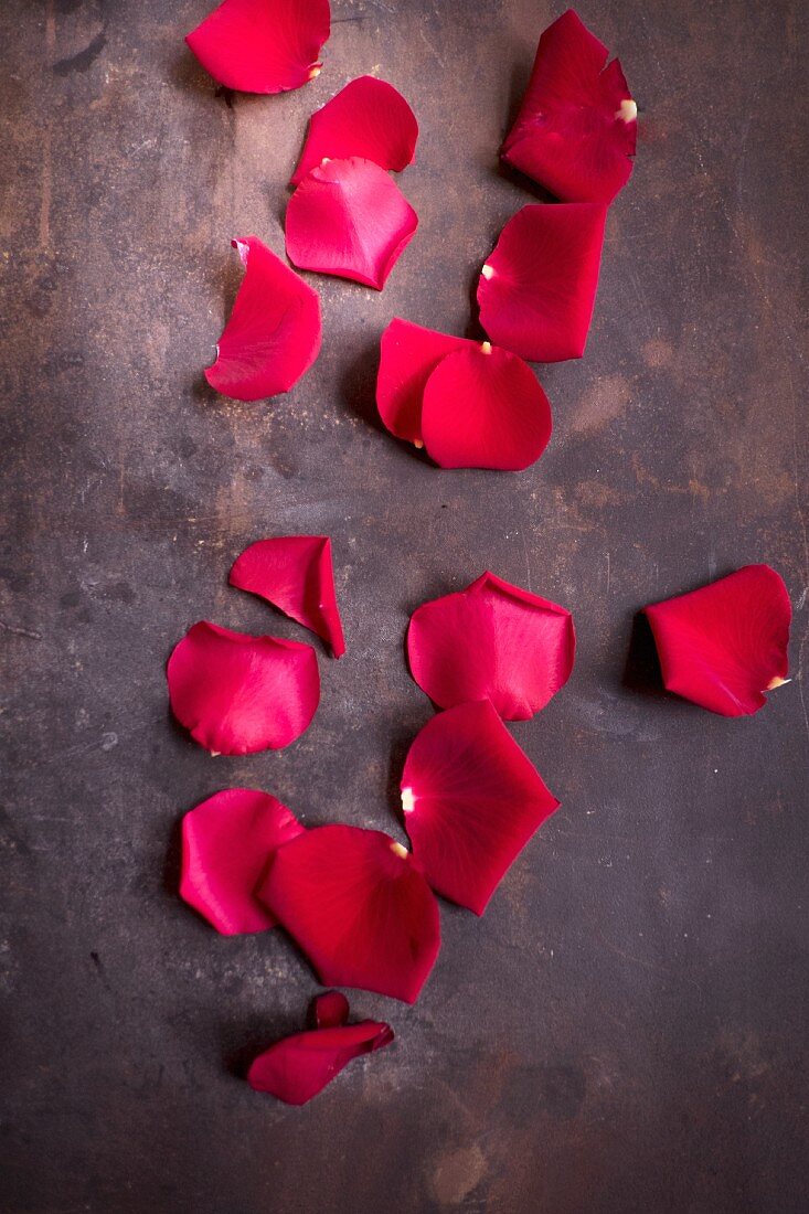 Red rose petals on brown surface (top view)
