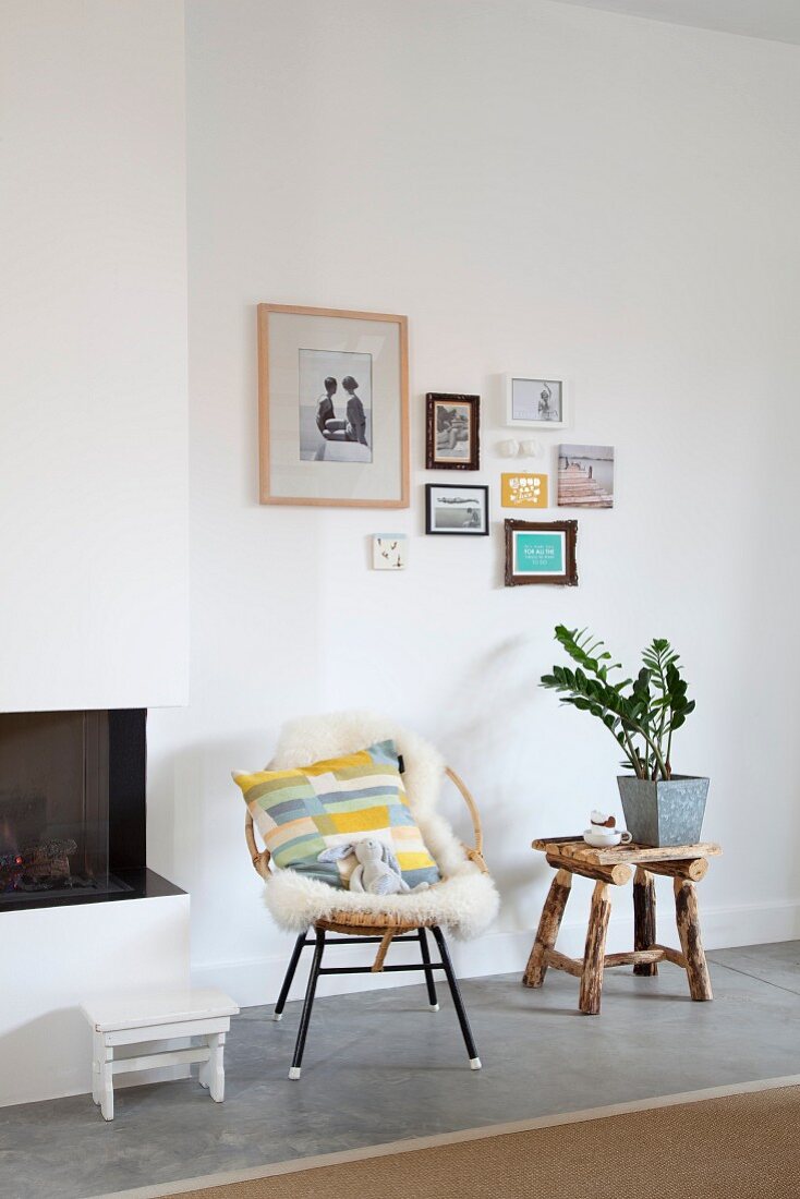 Sheepskin on easy chair and plant on stool below pictures on wall