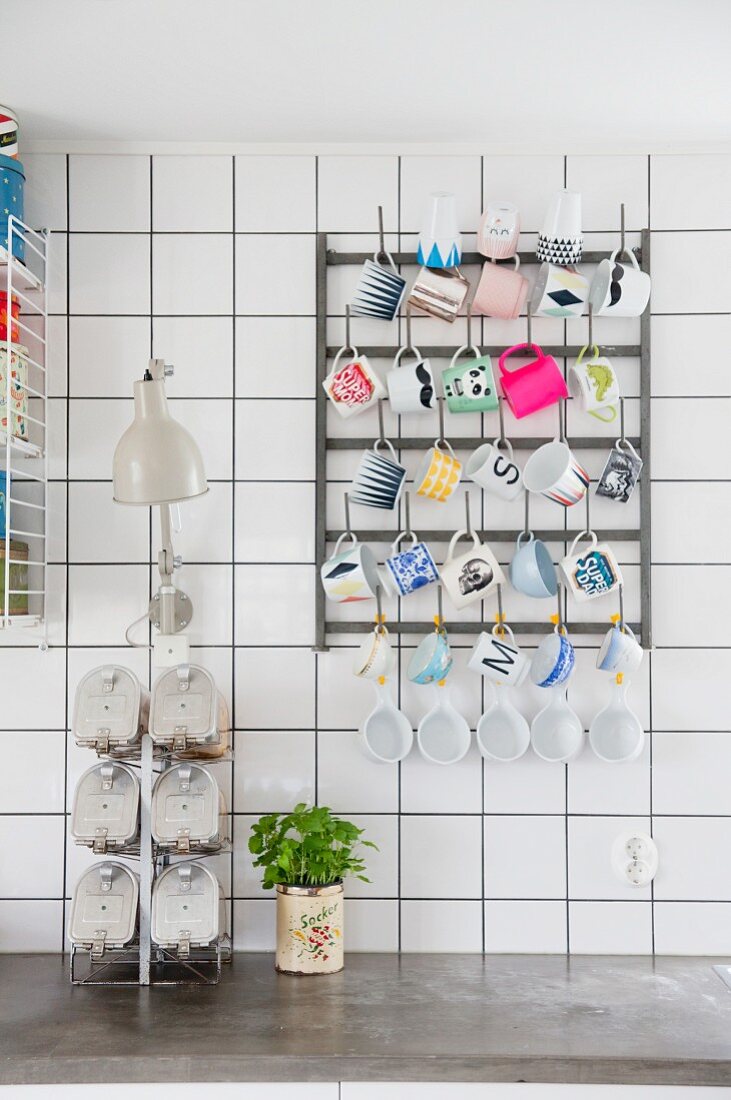 Various cups hung on rack mounted on white-tiled wall
