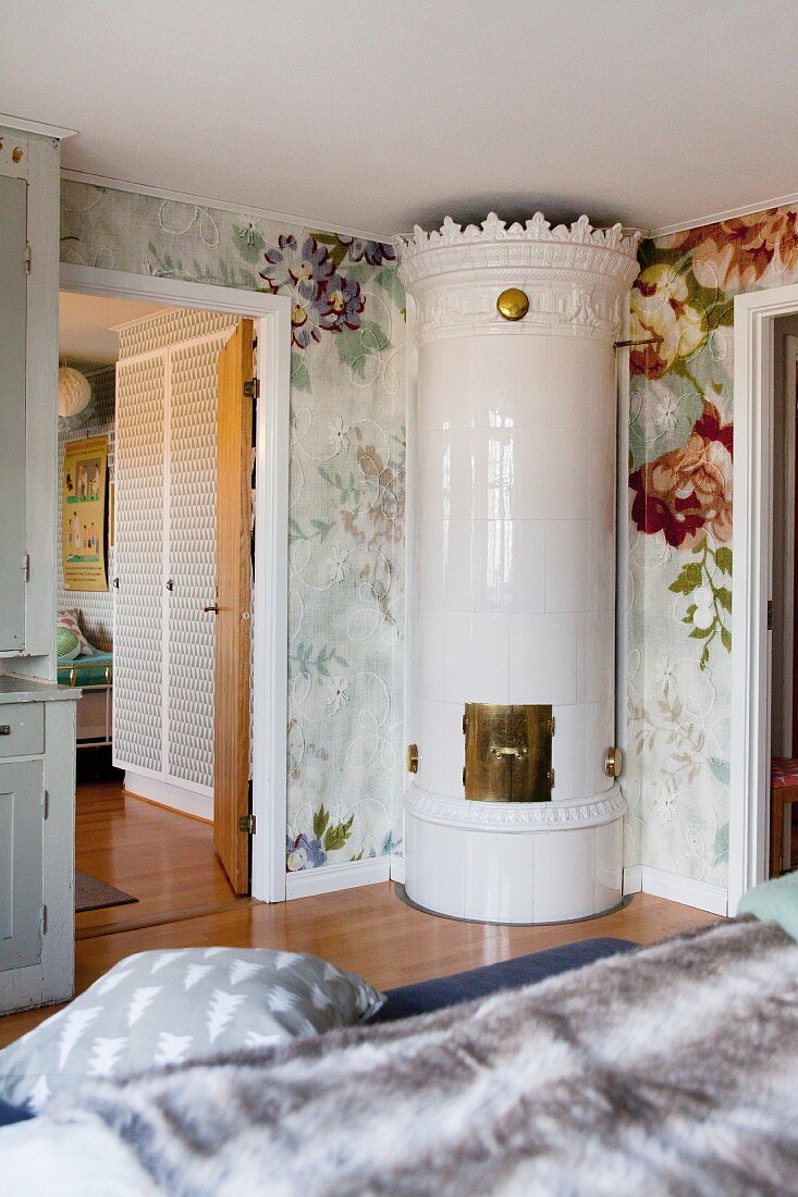 Elegant hand-crafted tiled stove in corner of bedroom with floral wallpaper