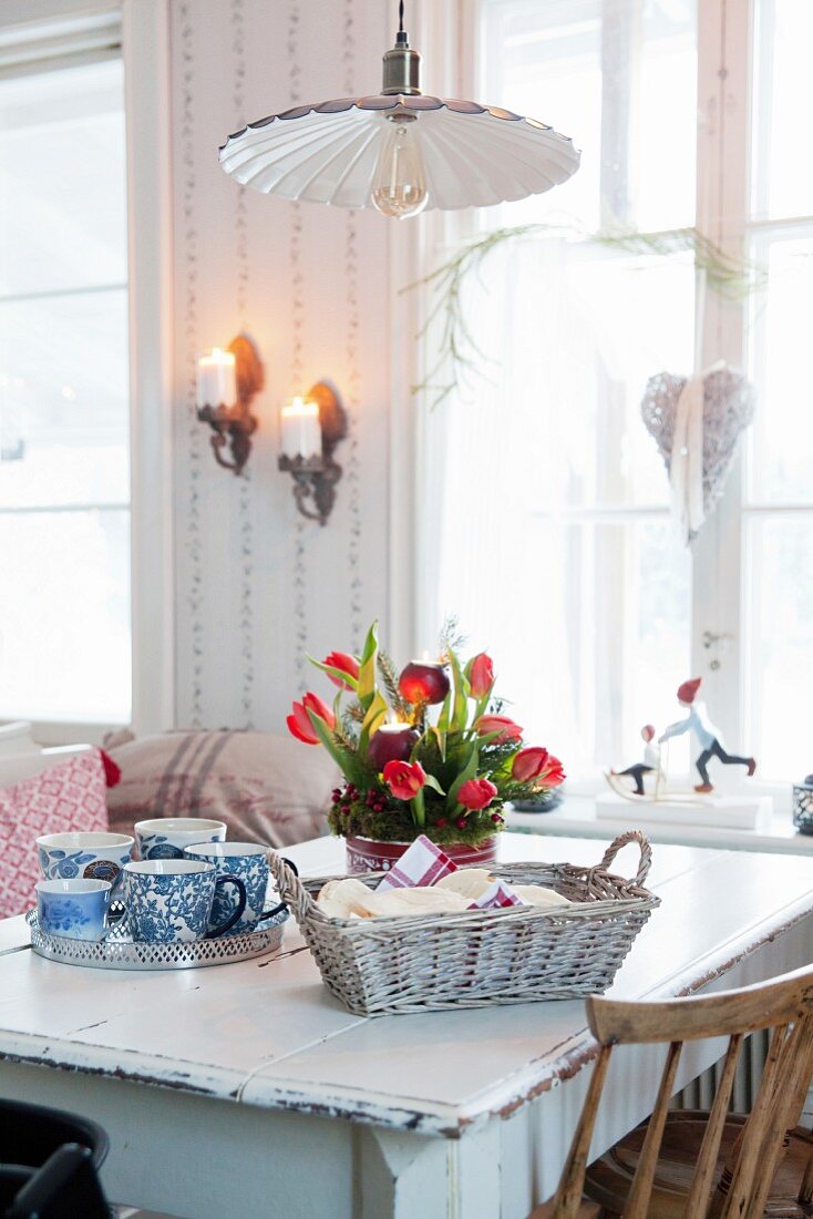 Adventsgesteck mit roten Tulpen auf Vintage Esstisch neben Brotkorb und Tablett mit Tassen