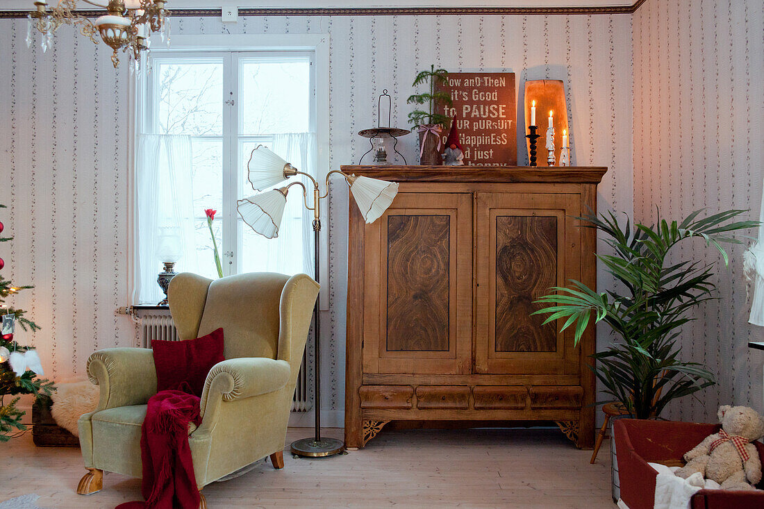 An old winged armchair in front of an antique wooden cupboard