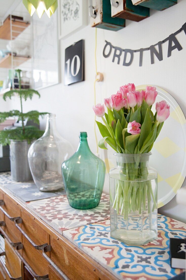 Glass vase of tulips on colourful cement-tiled top of retro sideboard