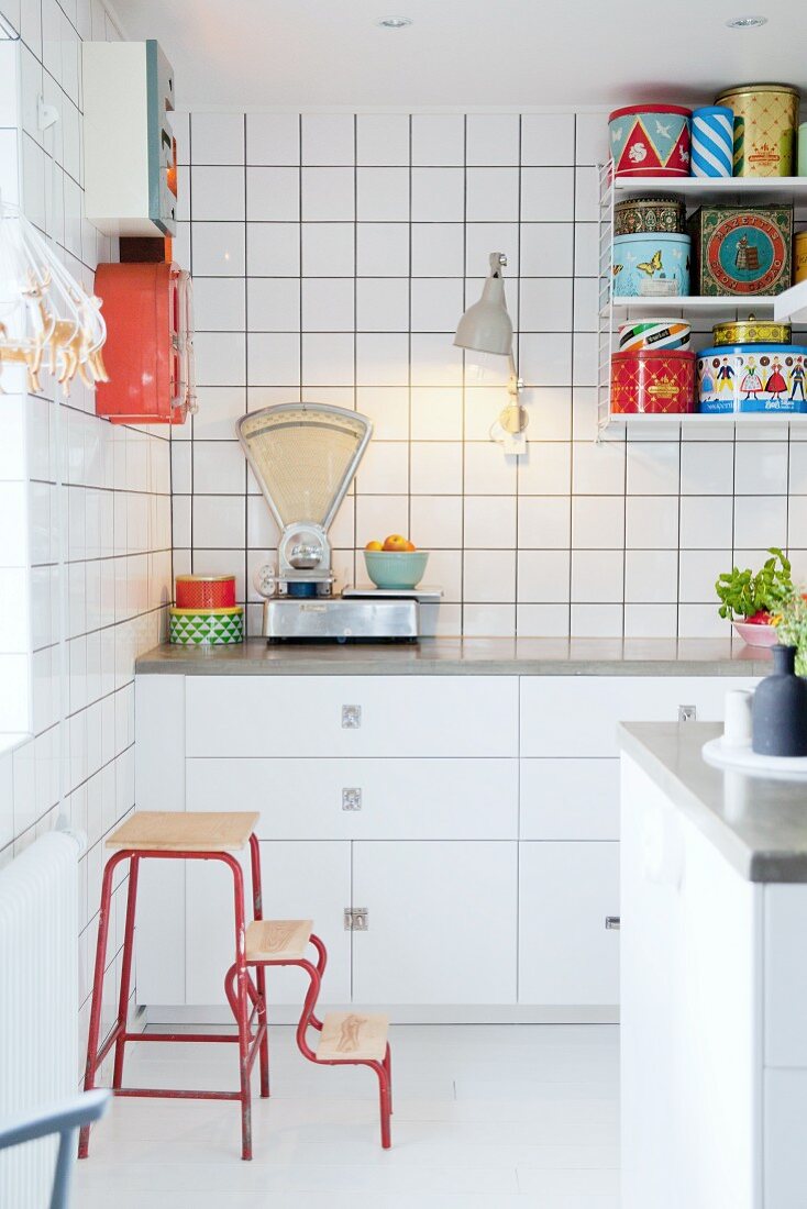 Retro scales and colourful tins in white fitted kitchen on String shelves