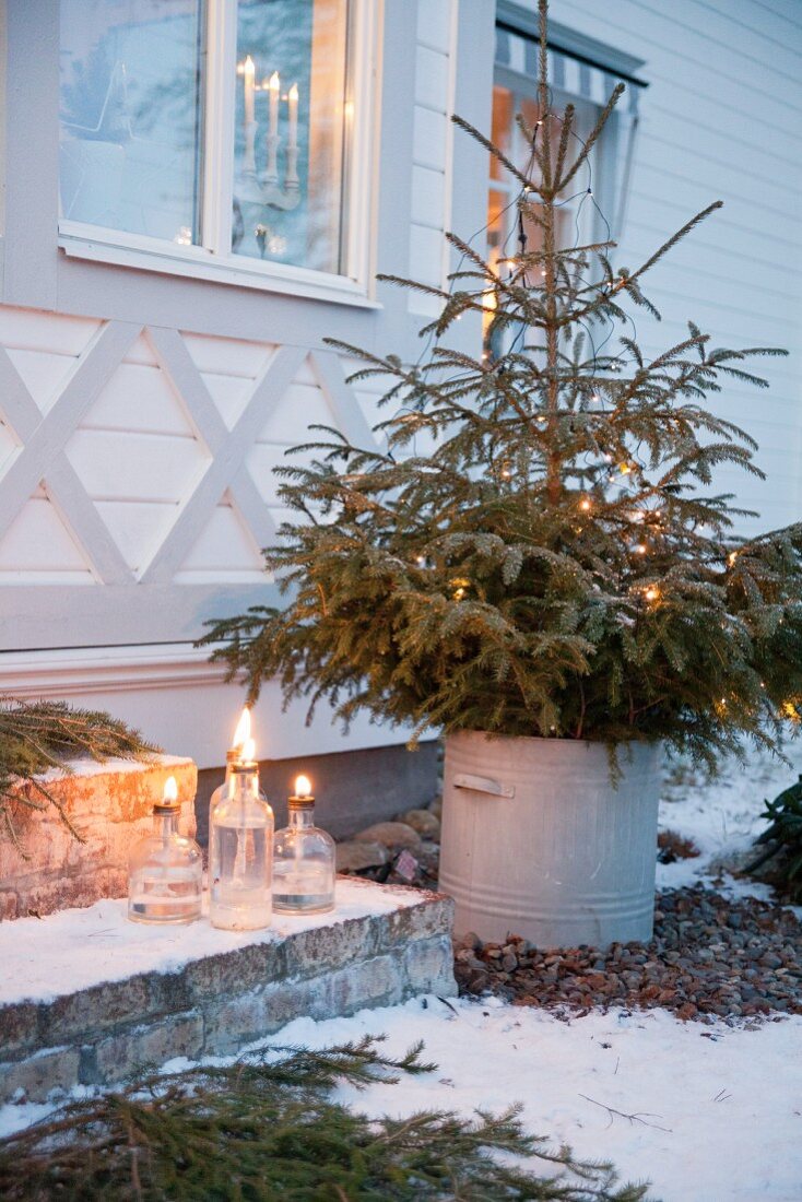 Tannenbaum im Metalleimer vor dem weihnachtlichen Schwedenhaus