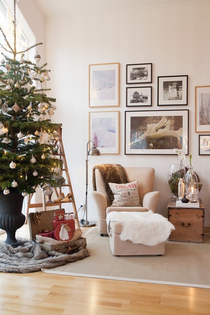 Geschmückter Weihnachtsbaum im Wohnzimmer mit beigem Sessel, Fusshocker und gerahmten Bildern an der Wand