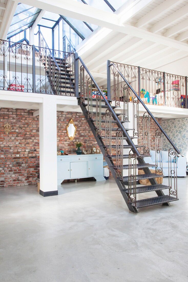 Steel stairs leading to two gallery levels in loft apartment with concrete floor and rustic brick wall