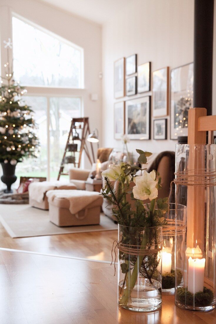 Christrosen in Glasvase und Windlichter auf Holzboden, im Hintergrund Wohnzimmer mit geschmücktem Weihnachtsbaum