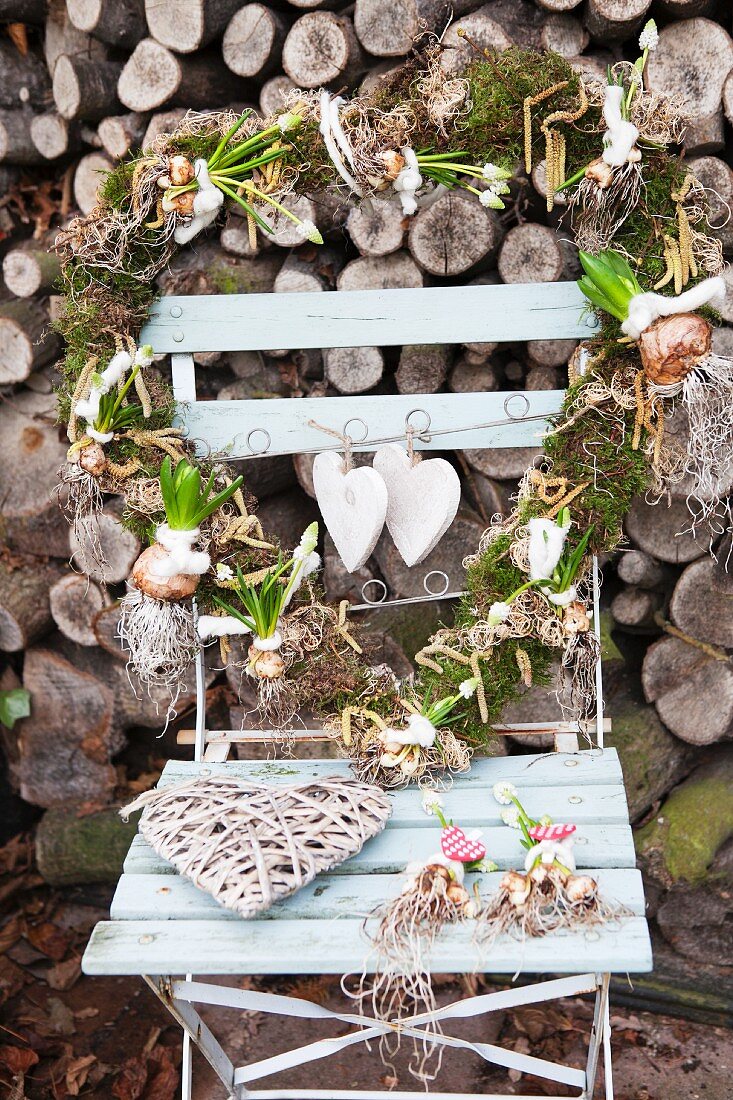 Herzförmiger Kranz mit Zwiebelblumen auf Gartenstuhl vor Brennholzstapel