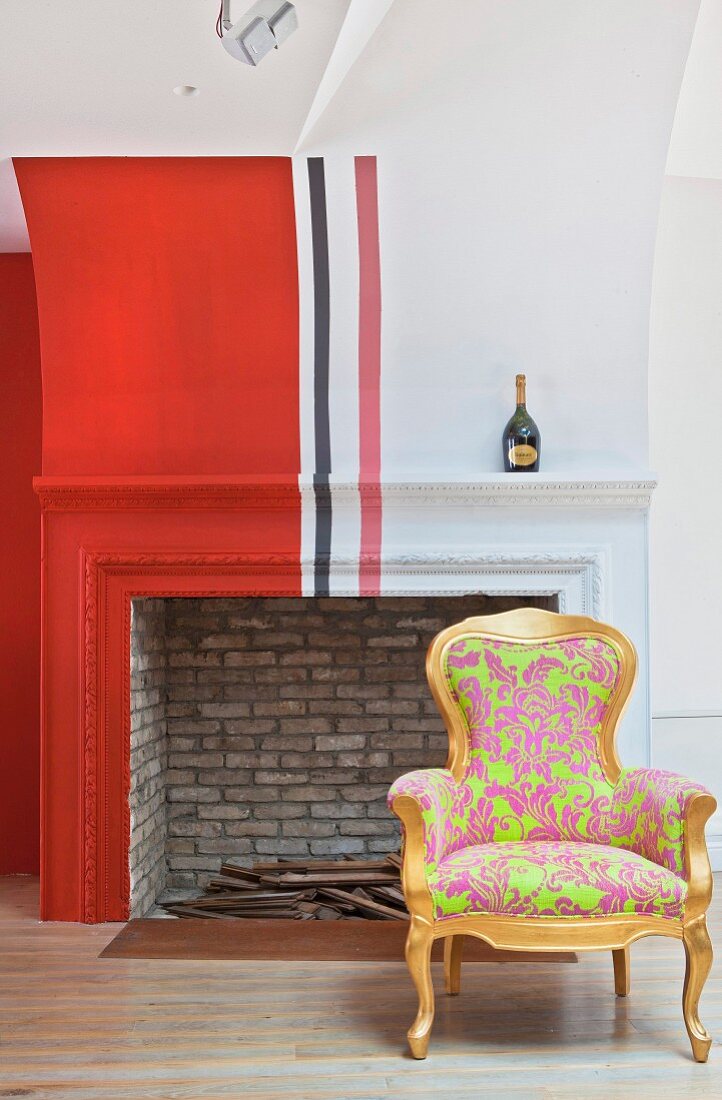 Antiker Sessel mit Bezug in Leuchtfarben vor Kamin mit rotem Anstrich