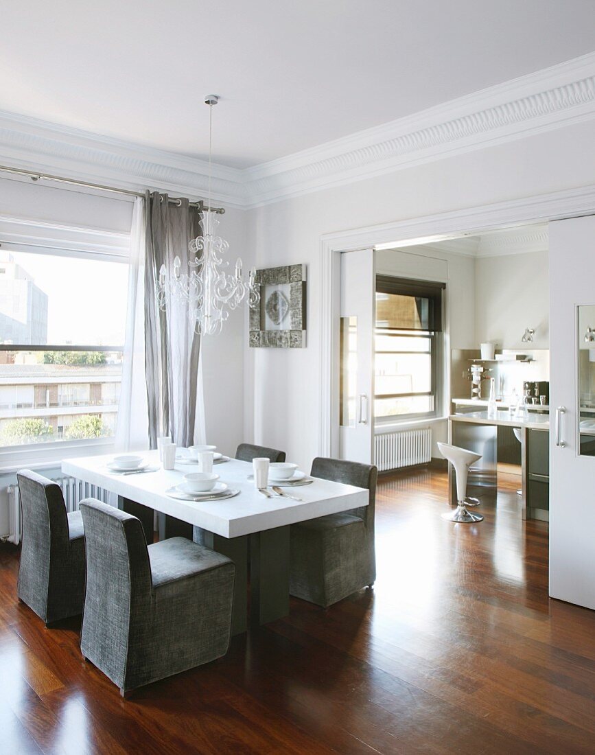 Weisser Esstisch mit grauen Hussenstühlen vor Fenster in elegantem Esszimmer mit Schiebetür