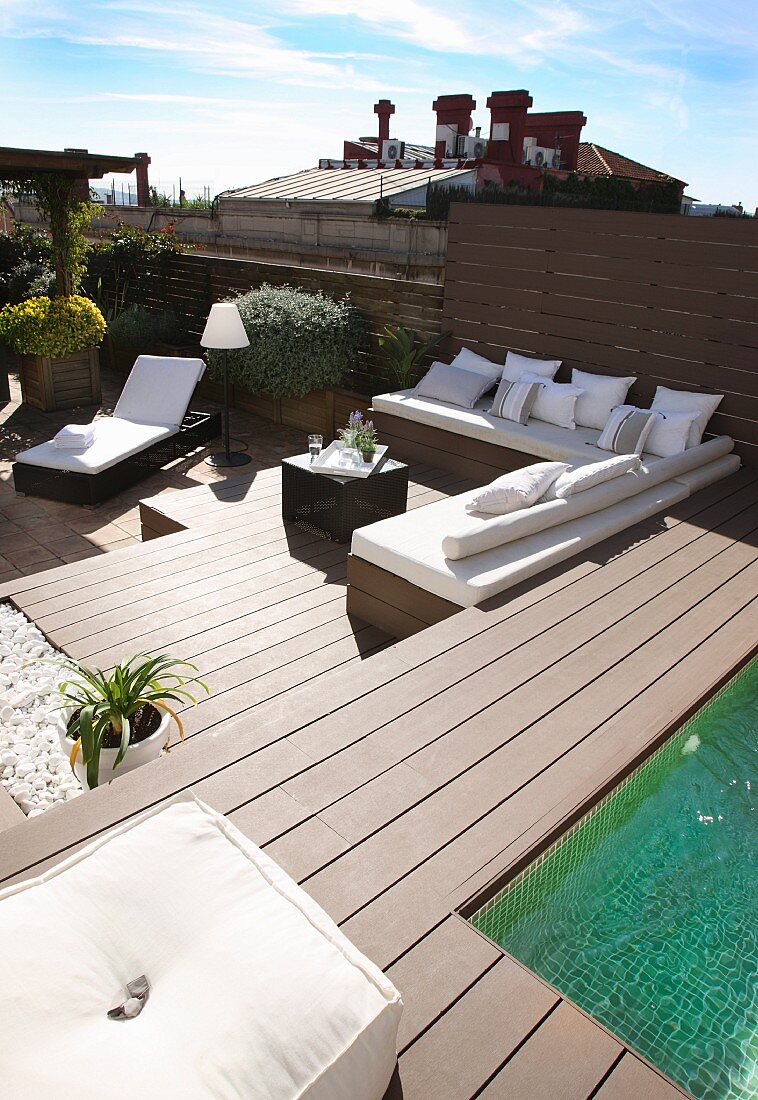 Elegant lounger and benches with white cushions on sunny roof terrace with pool
