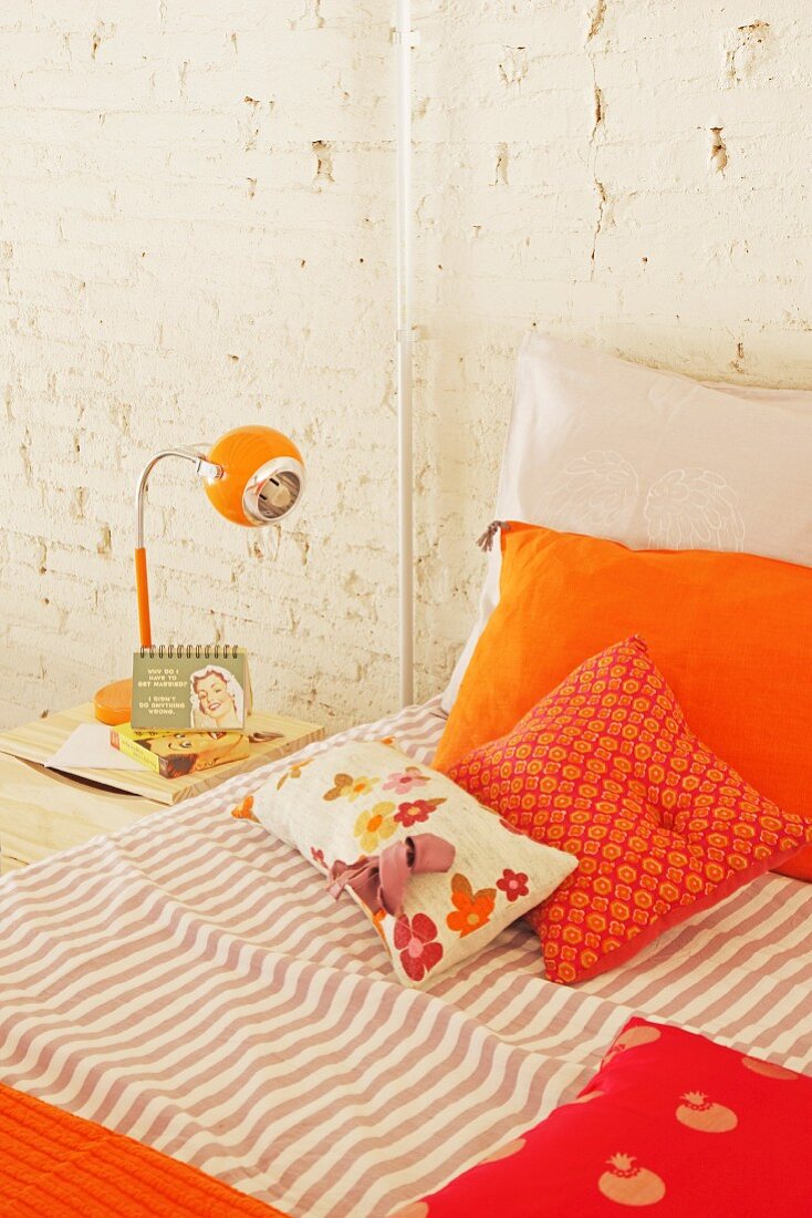 Bett mit orangefarbenen Kissenbezügen und Nachttischlampe im Retrolook