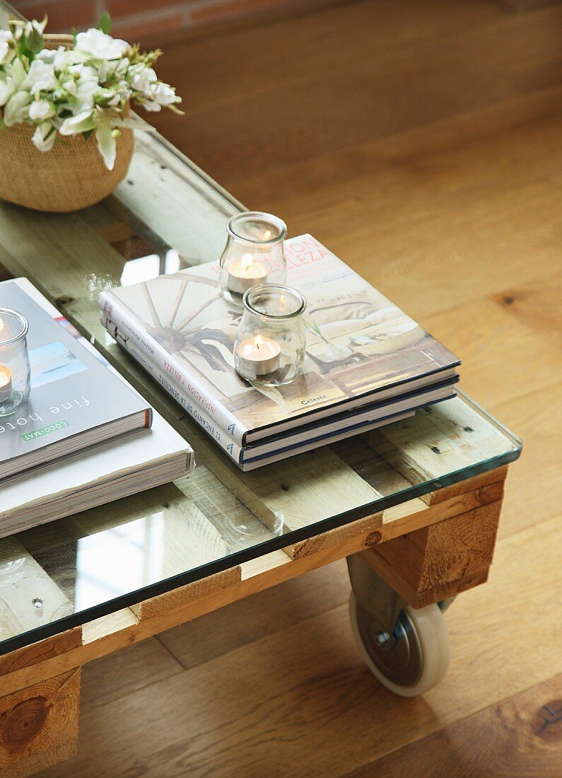 Bücher und Teelichtgläser auf rollbarem Palettentisch mit Glasplatte