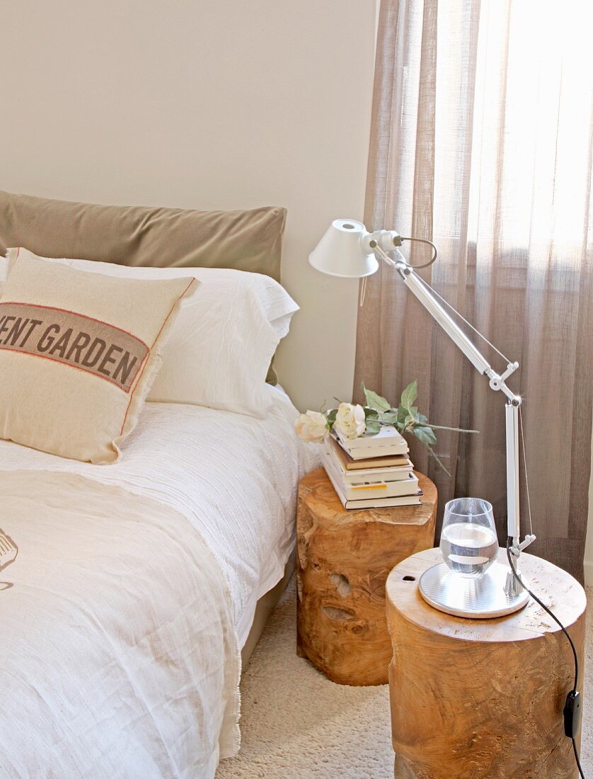 Baumstamm-Hocker als Nachttische mit Bücherstapel und Tischleuchte neben Doppelbett