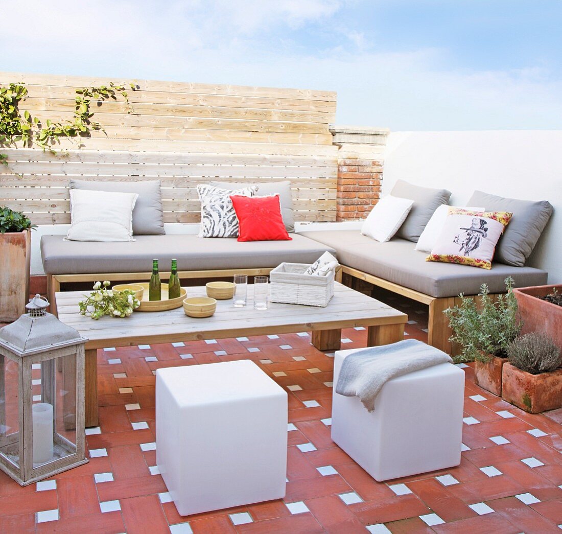 Terracotta tiles, upholstered outdoor furniture and cubic pouffes on summery terrace