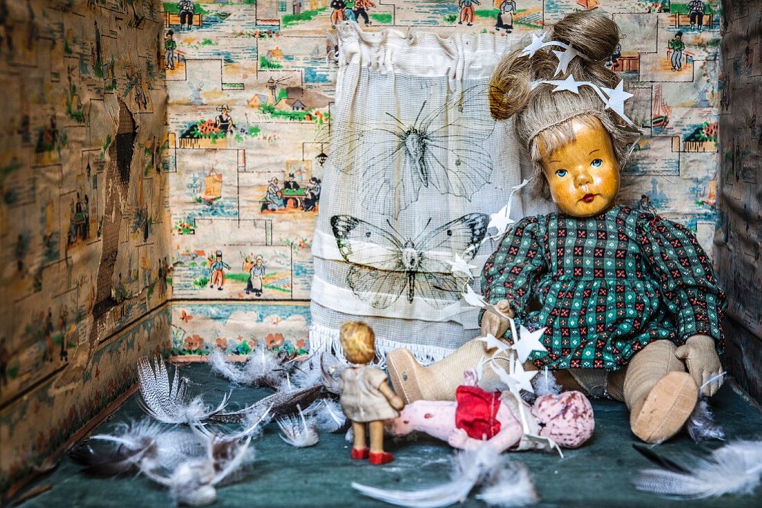 Feathers and antique dolls in box with sides covered in torn paper