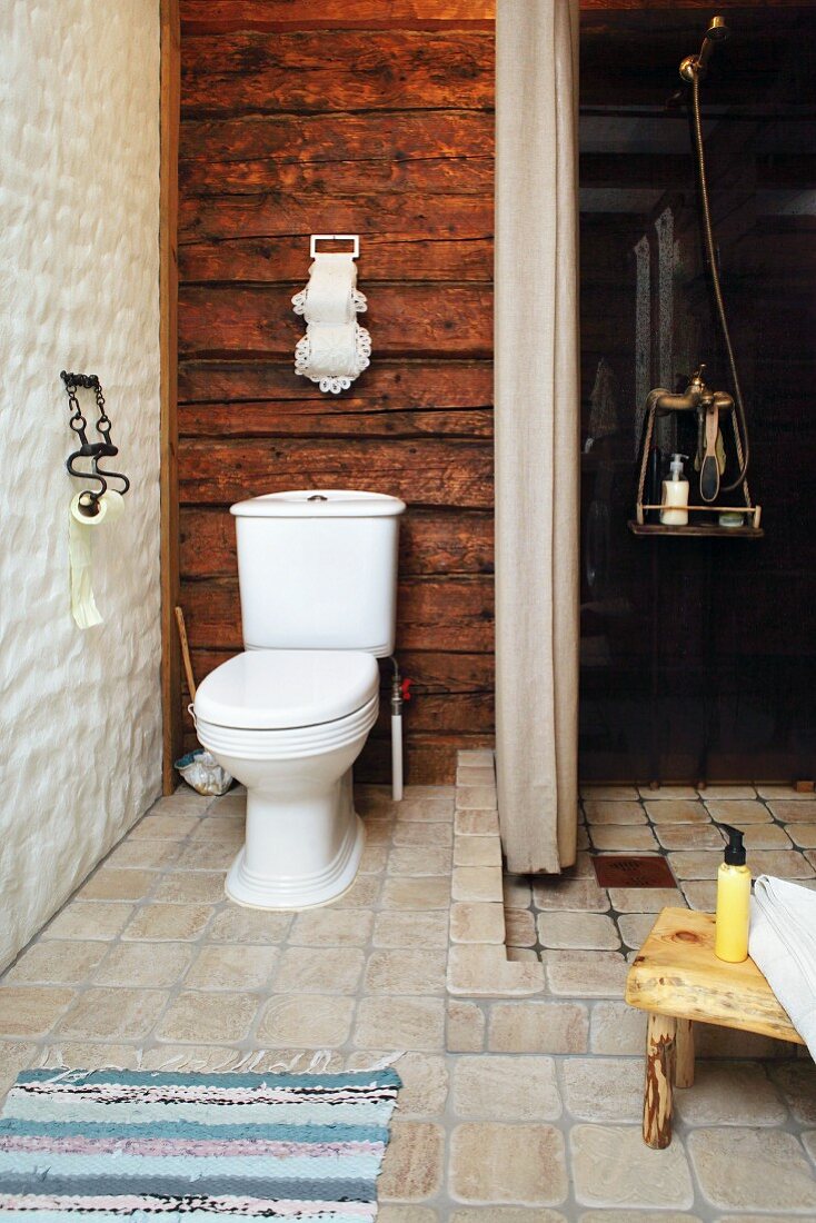 Toilette vor rustikaler Holzwand neben offener Dusche