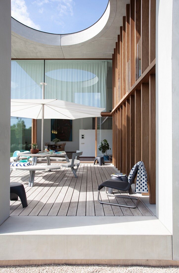 Outdoor furniture on roofed wooden terrace with skylight outside architect-designed house