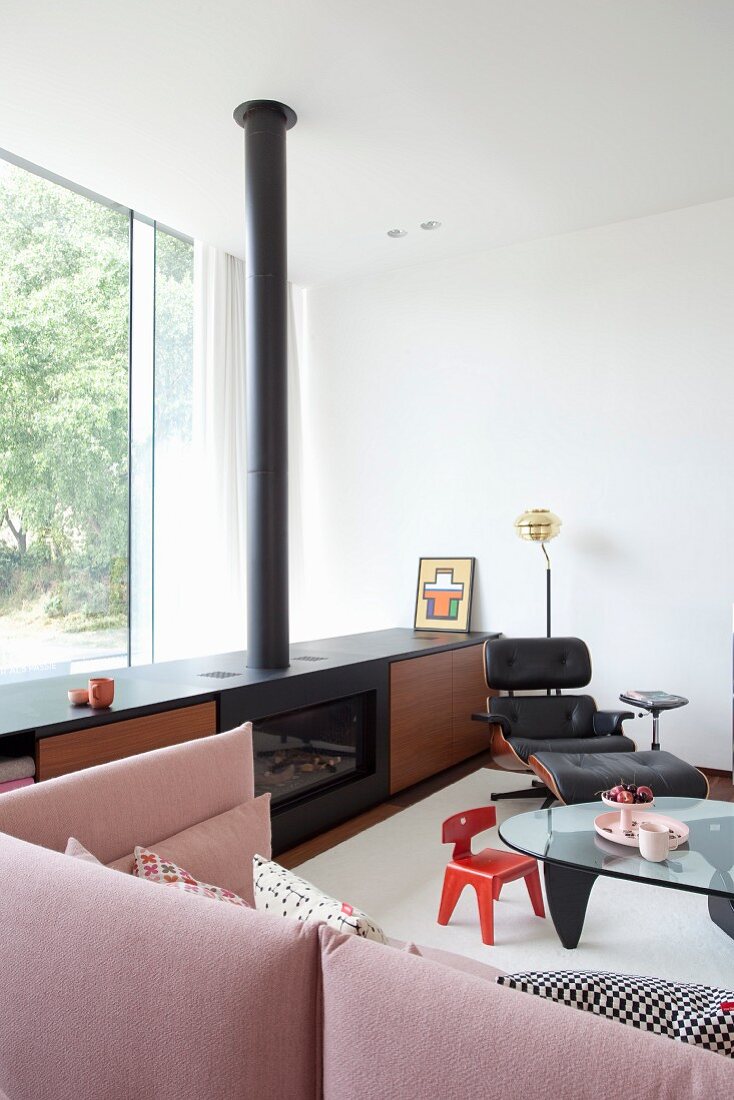 Sideboard mit eingebautem Kamin, Lounge Chair, Kinderstuhl um Coffeetable mit Glasplatte und altrosa Couch in eleganter Lounge