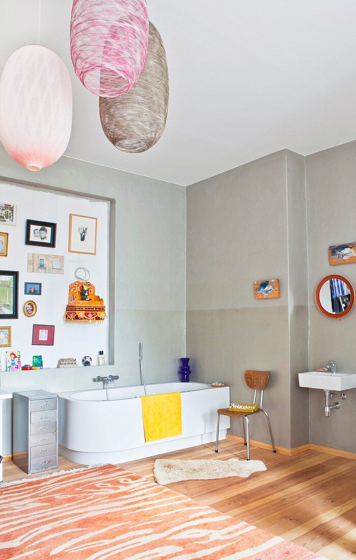 Bathtub, wall decorated with various items and designer pendant lamps in spacious bathroom of period apartment