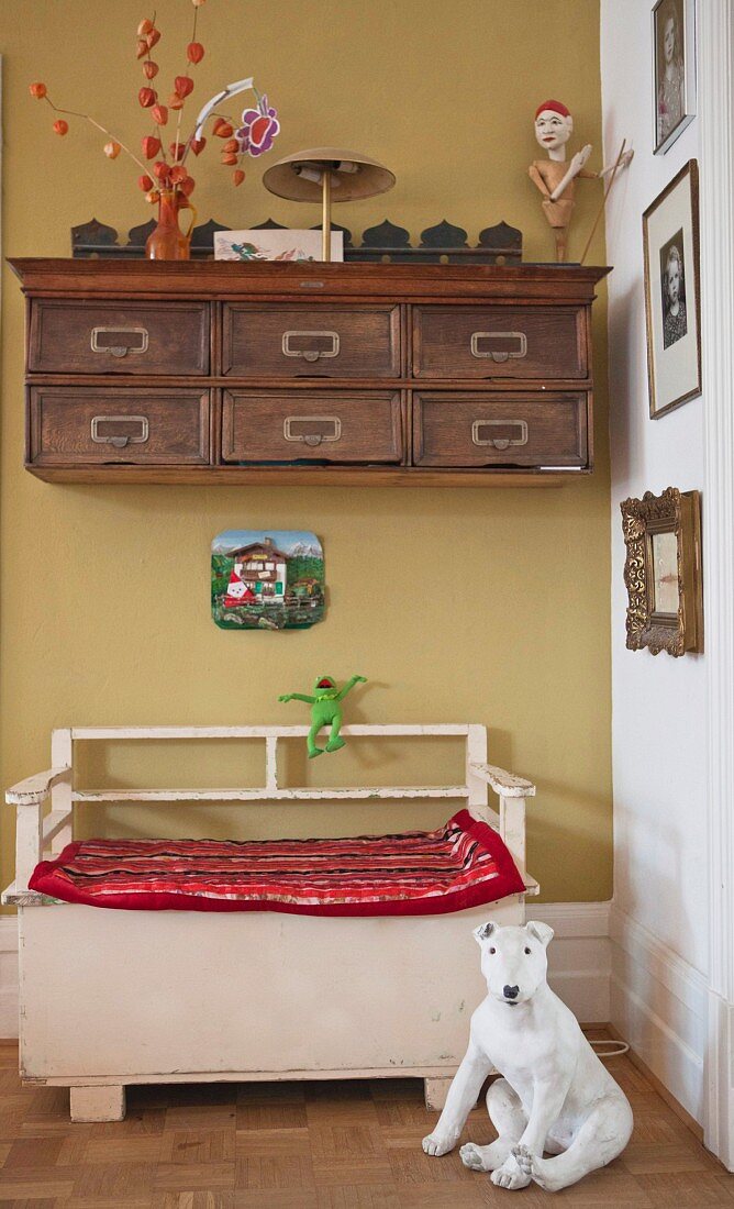 Dog ornament in front of vintage wooden bench below antique wall-mounted cabinet in hallway