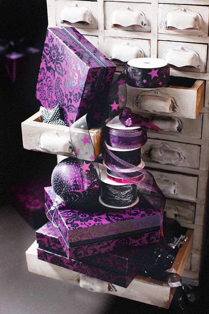 Violette Schachteln und Seidenband auf einem Schubladenschränkchen