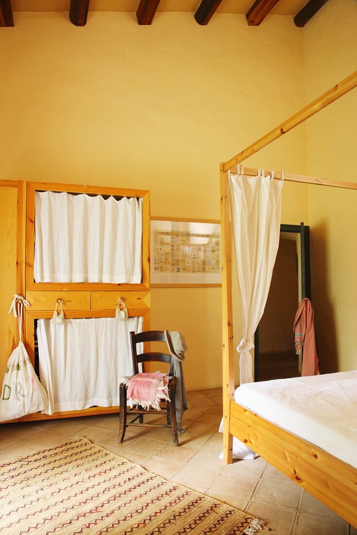Wooden furniture and four-poster bed in yellow-painted bedroom