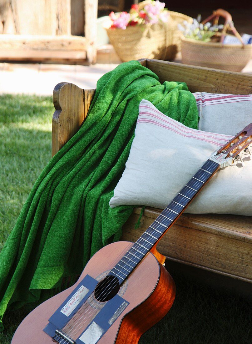Guitar leaning against wooden bench with cushions and green blanket