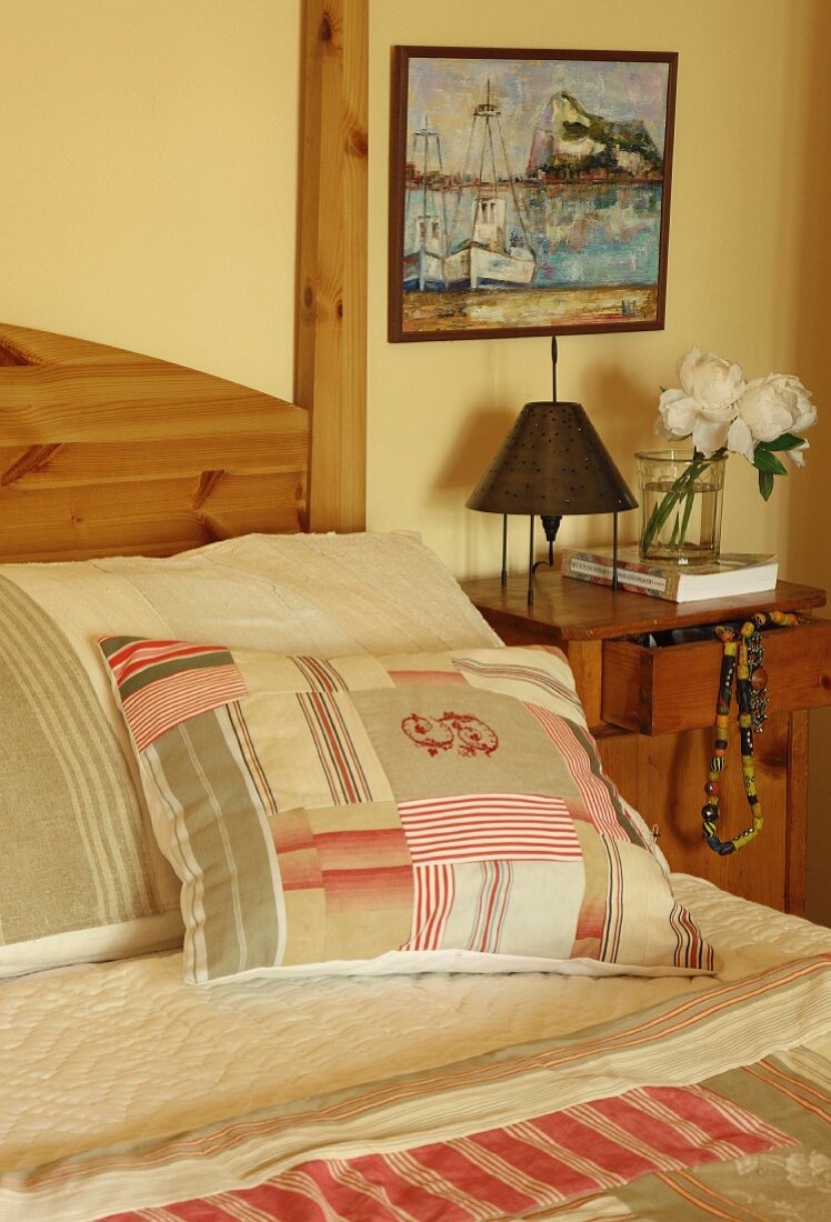 Patchwork scatter cushions on bed next to bedside table and painting
