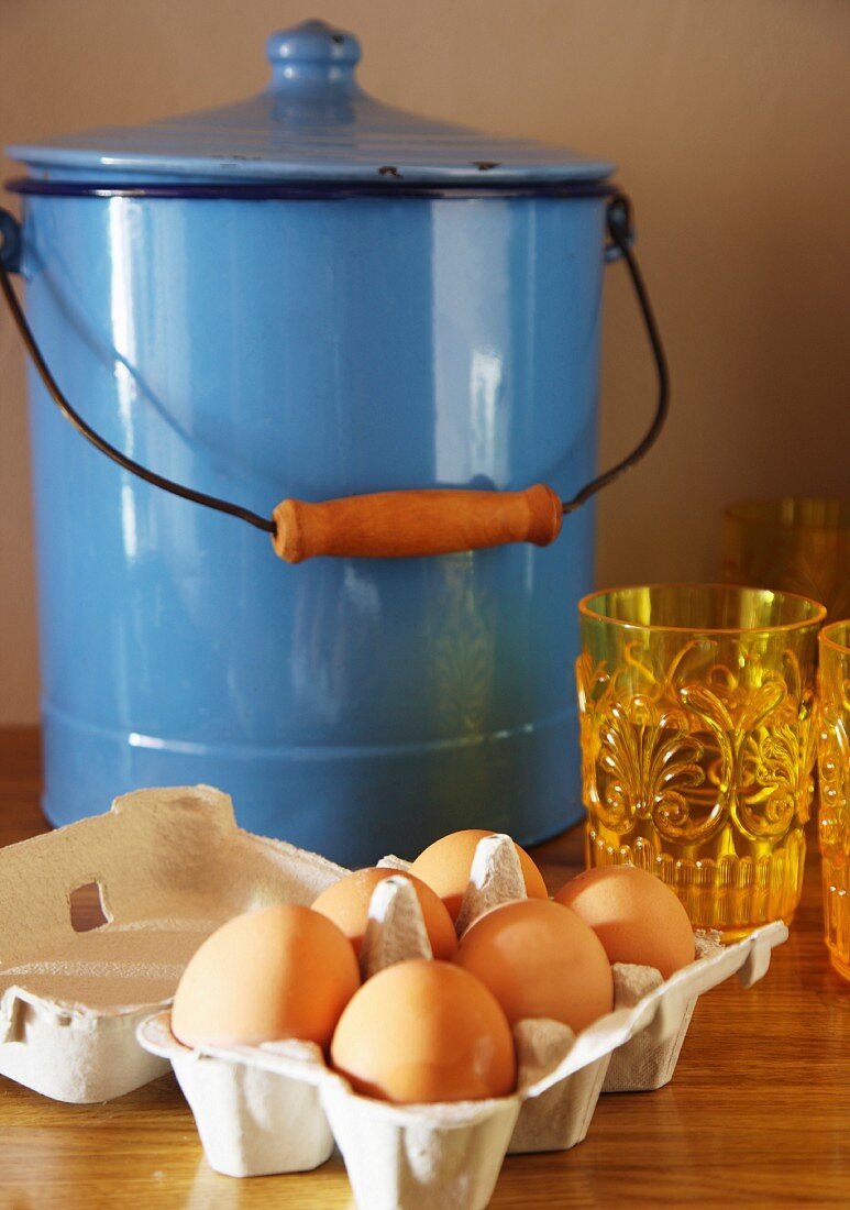 Eggs in egg boy in front of blue enamel bucket with lid