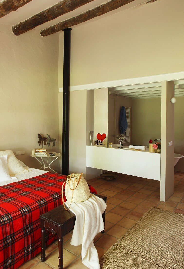 Blick von Schlafzimmer mit rot karierter Tagesdecke in Bad Ensuite mit schlichtem Einbauregal