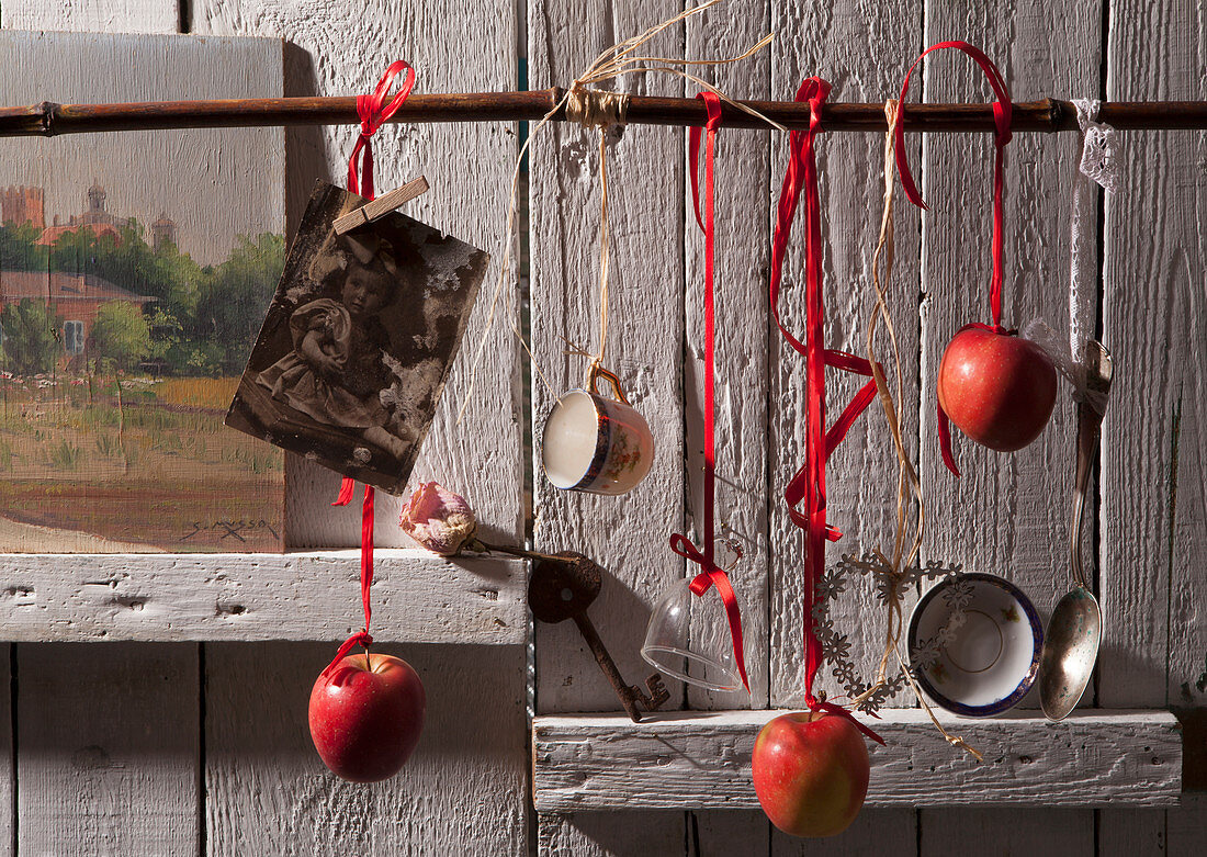 Aufgehängte rote Äpfel und alte Küchenutensilien vor Holzwand