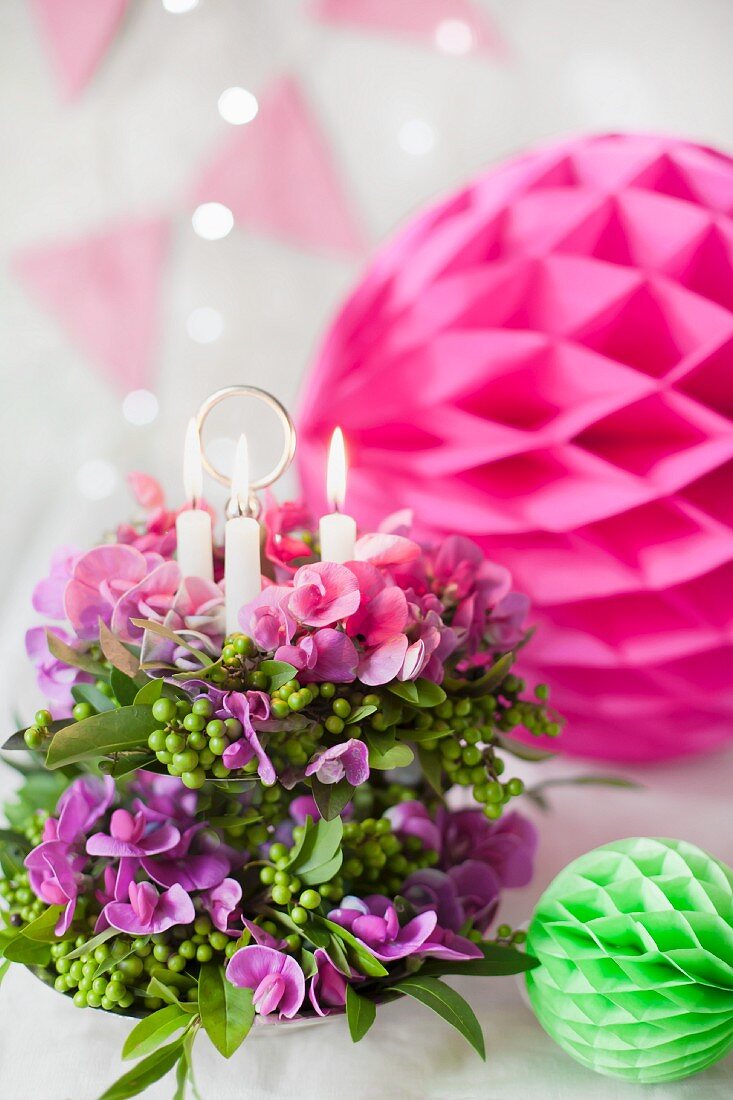 Blumengesteck mit Kerzen auf Etagere und bunte Wabenbällchen