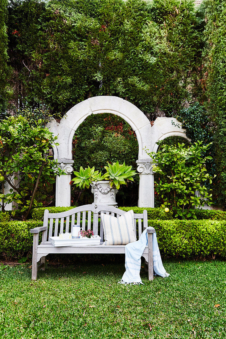 Wooden bench in a well-tended garden, arched in the background