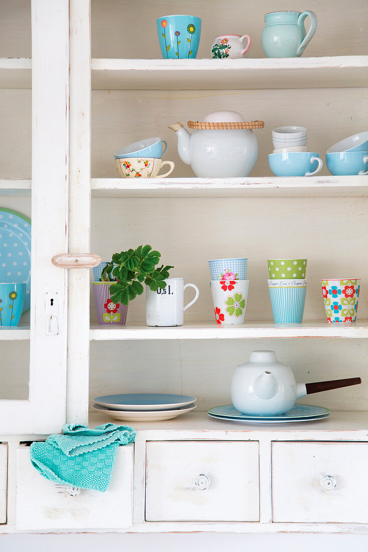 Colourful mugs and teapots in white cupboard